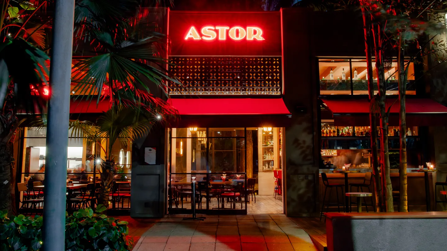 Fachada do Bar Astor à noite, com letreiro em neon e toldo vermelho