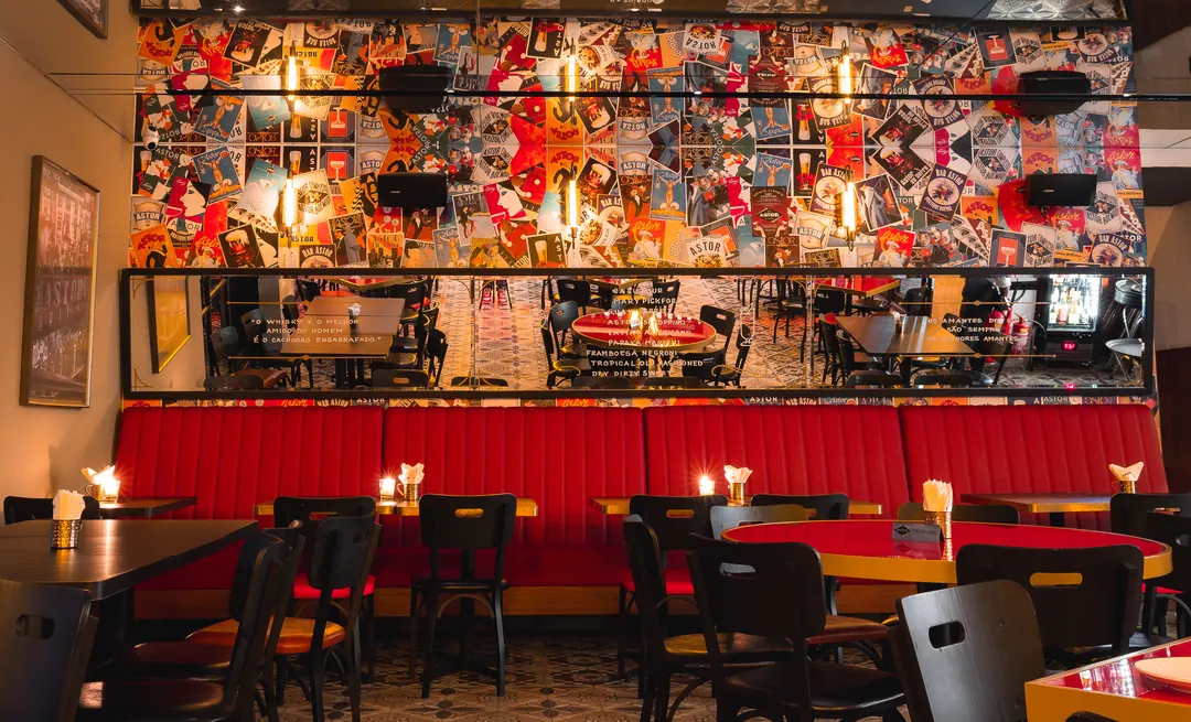 Banco estofado vermelho sob painel de colagens