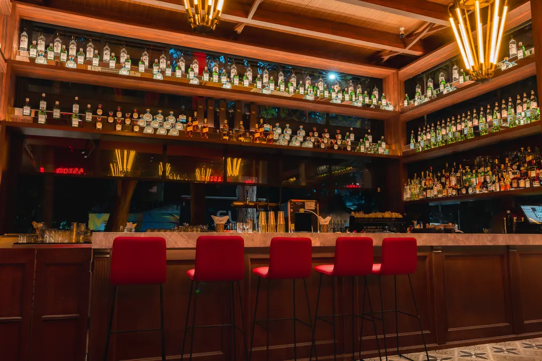 Bar com prateleiras de garrafas e banquetas vermelhas