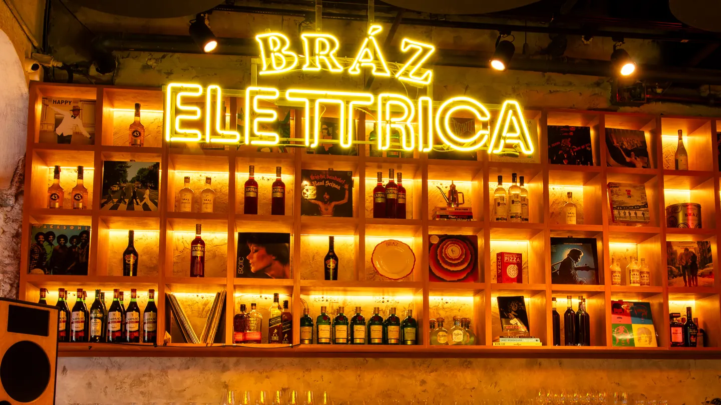 Letreiro Bráz Elettrica em neon sobre estante iluminada de garrafas e discos