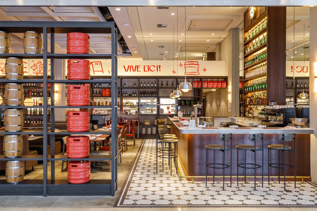 Bar com estante de garrafas e caixas vermelhas junto à entrada