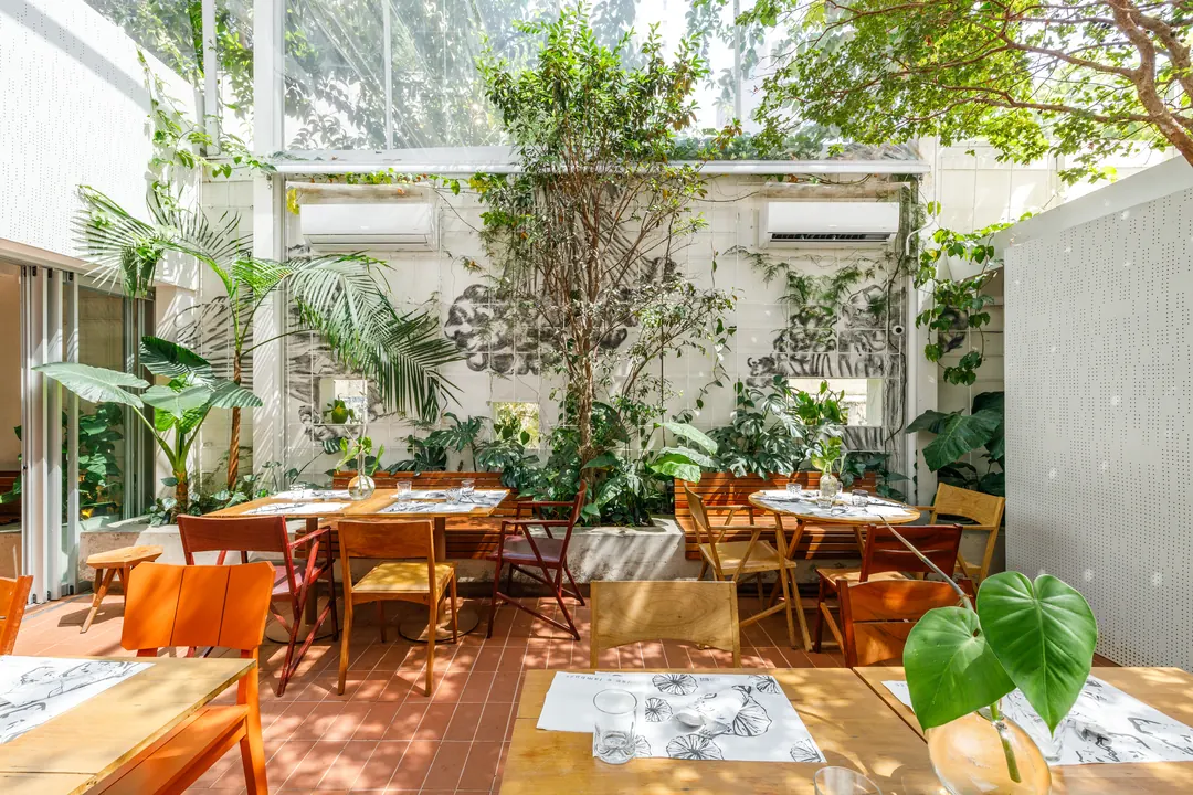 Pátio do Just a Bite com cobertura de vidro, árvore e mesas de madeira