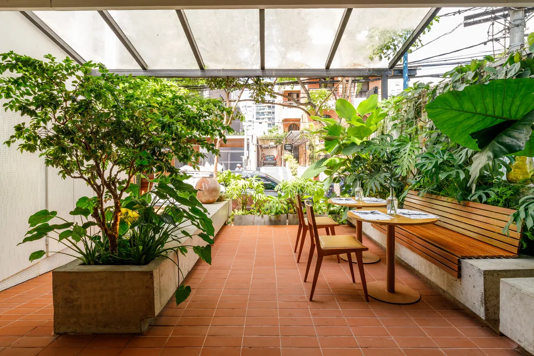 Área externa com vasos de concreto e mesas junto à vegetação
