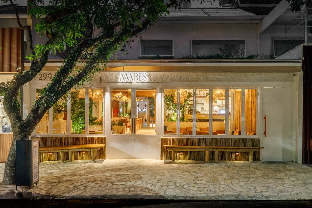 Fachada do Mares à noite, com árvore na calçada e salão iluminado