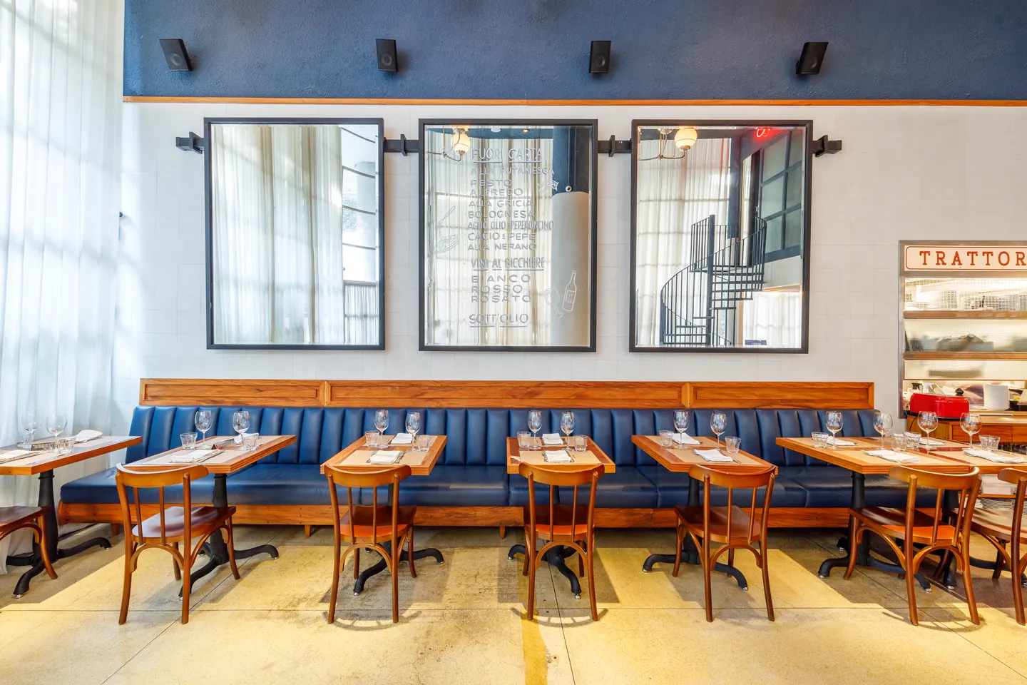 Salão da Tappo Trattoria com banco estofado azul, espelhos e mesas de madeira