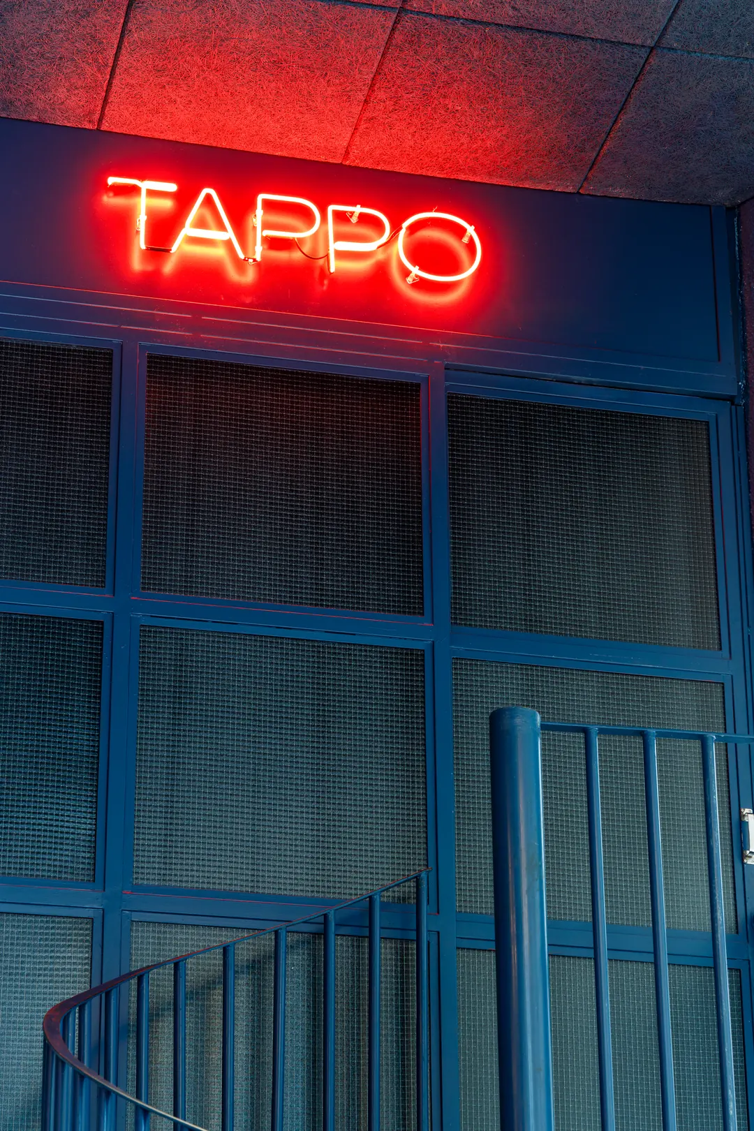 Letreiro em neon vermelho da Tappo sobre porta de vidro